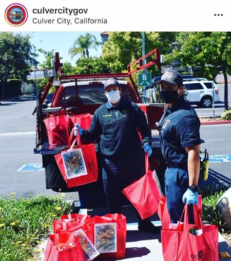 Photograph of Culver City firemen loading emergency food bags with artwork attached into vehicle for delivery 