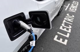 Photograph of side of white car with electric charging cord attached, parked in electric vehicle parking space