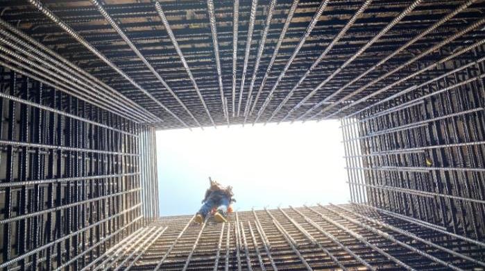 Photograph looking up a deep shaft showing worker tying rebar