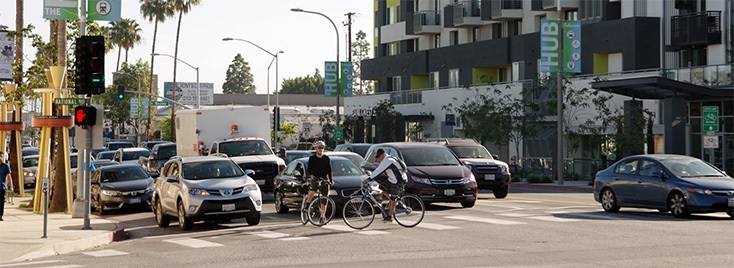 Photograph of multiple cars and bikes stopped at downtown Culver City intersection.